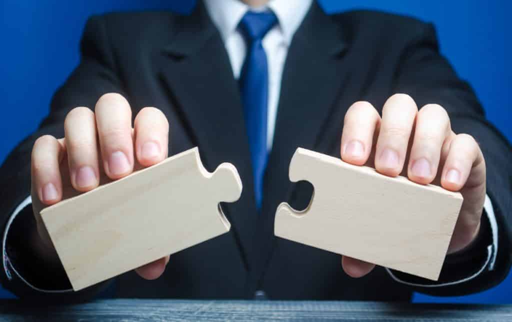 Businessman holds two empty puzzle pieces to illustrate a merger.