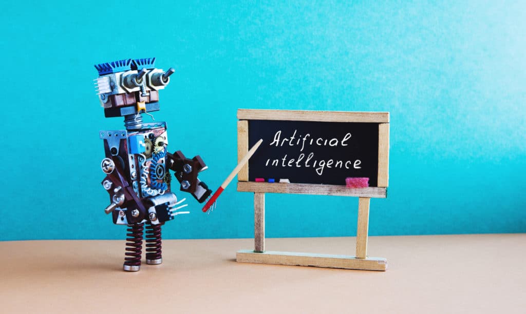 Robot teacher points to a chalkboard with the word Artificial Intelligence written on it